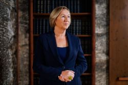 Professional woman in a navy blazer standing in a library alcove, thoughtful expression.