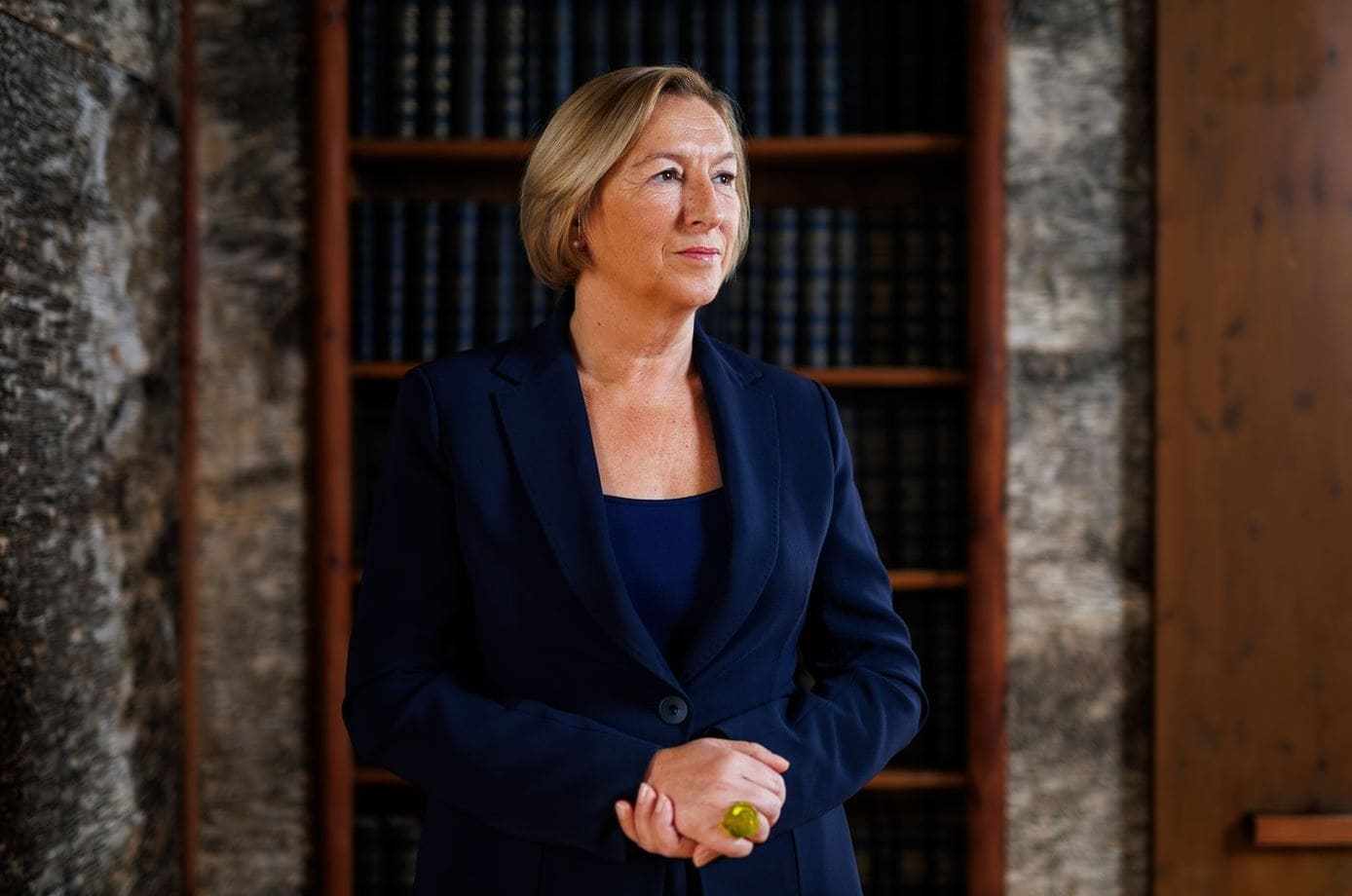 Франция готова к оборонному сотрудничеству | Наш Ванкувер Professional woman in a navy blazer standing in a library alcove, thoughtful expression.