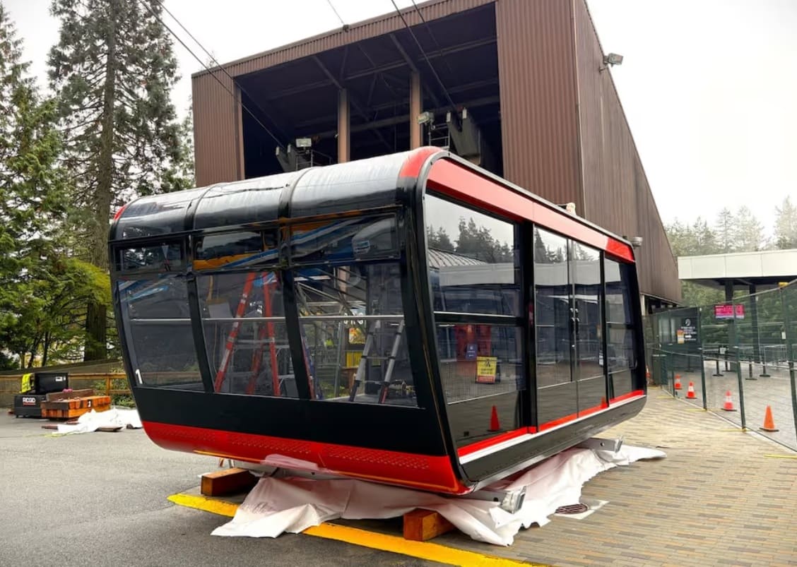 кабины grouse | Наш Ванкувер Gondola cabin under installation at a station, black and red exterior with glass walls and scaffolding visible nearby.