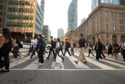 Crowded city crosswalk with pedestrians crossing a wide street amid tall buildings.