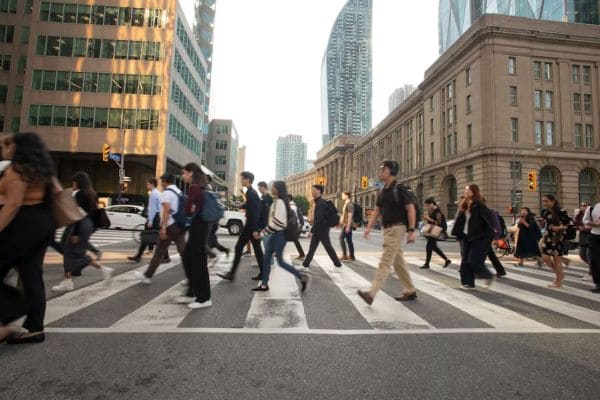 Crowded city crosswalk with pedestrians crossing a wide street amid tall buildings.