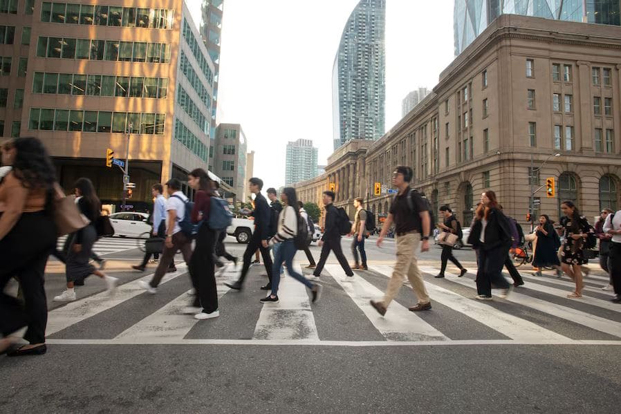 Канада меняет систему баллов | Наш Ванкувер Crowded city crosswalk with pedestrians crossing a wide street amid tall buildings.