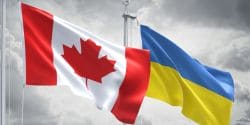 Canadian and Ukrainian flags fluttering together in the wind against a cloudy sky, symbolizing solidarity.