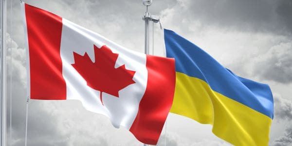 Canadian and Ukrainian flags fluttering together in the wind against a cloudy sky, symbolizing solidarity.