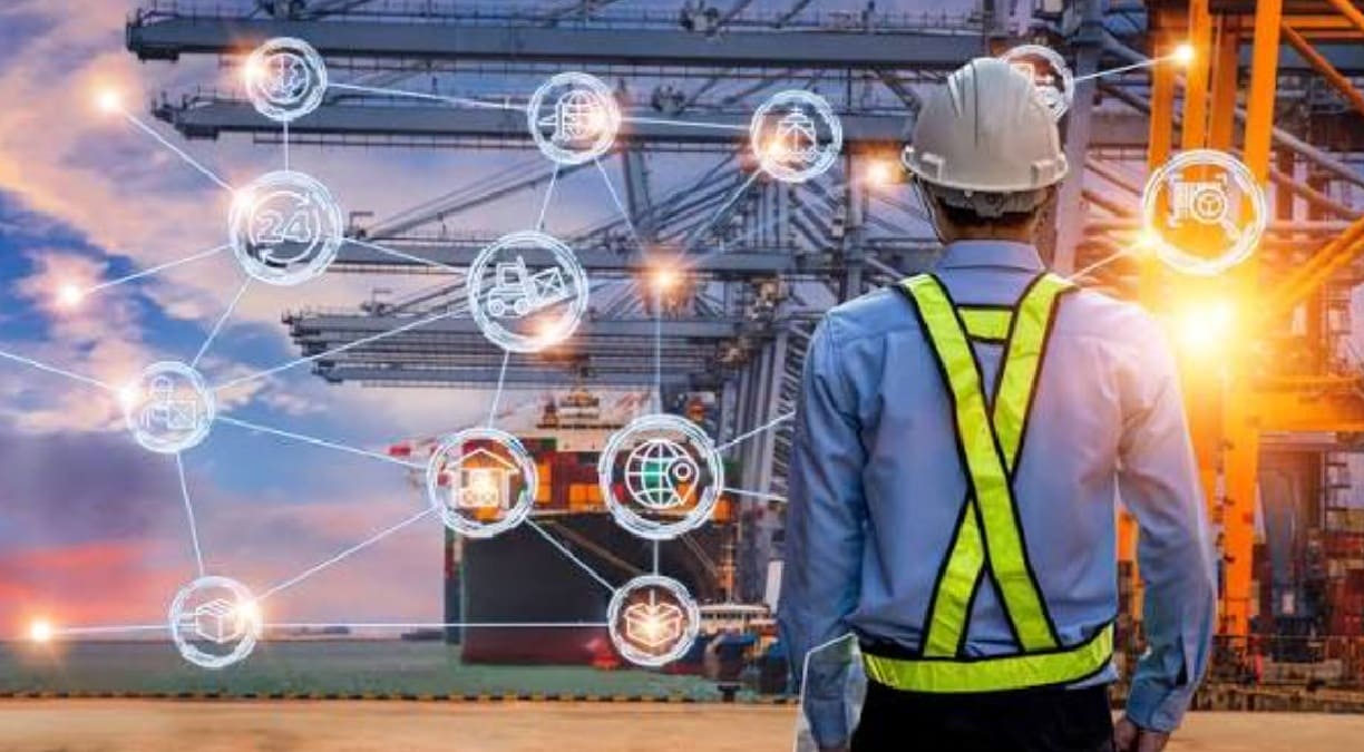Port worker with a safety vest and hard hat stands with back to camera, facing a cargo yard with a network of glowing holographic icons around him, symbolizing connected logistics.