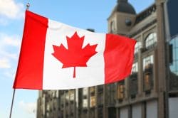 Canadian flag waving outdoors in front of urban buildings along a street.