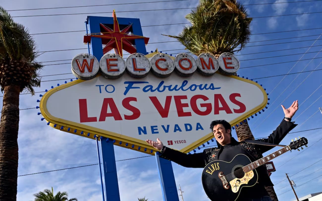 Elvis impersonator posing with a guitar beside the Welcome to Fabulous Las Vegas sign.