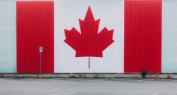 Large mural of the Canadian flag painted on a building, with red panels and a central white stripe featuring a red maple leaf, in a parking lot.