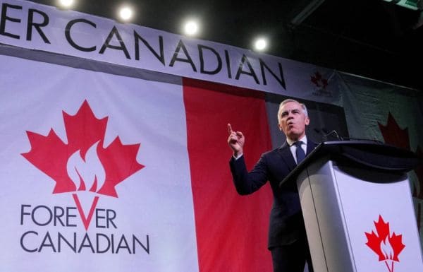 Politician in a dark suit giving a speech at a podium on a stage, with a large Canadian flag backdrop and the words 'Forever Canadian' visible.
