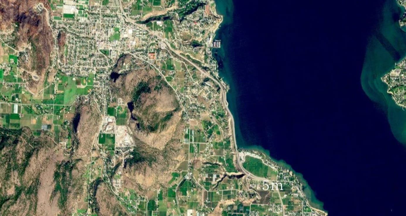 Satellite view of a coastal region with fields, towns and hills along a bay; a 5 m scale marker is visible near the shore.