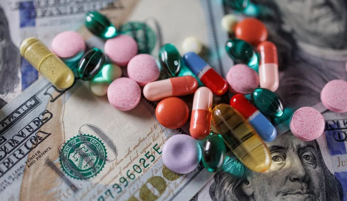 лекарства подорожают для американцев | Наш Ванкувер Colorful pills and tablets scattered over a pile of US $100 bills, suggesting drug trade or pharmaceutical costs.
