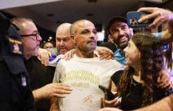 A group of people gathers around a man in a white Skechers shirt as someone takes a selfie with them, smiling and supportive reactions visible around him.