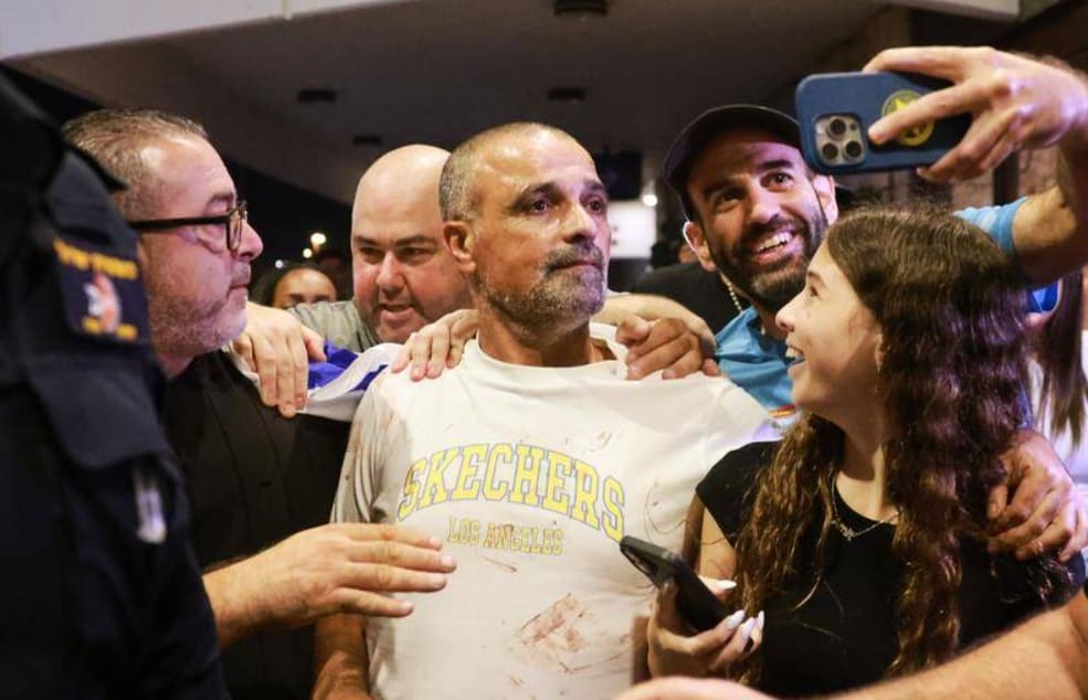 A group of people gathers around a man in a white Skechers shirt as someone takes a selfie with them, smiling and supportive reactions visible around him.