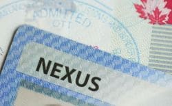 Close-up of a blue NEXUS travel card on top of a passport page with an 'ADMITTED' stamp and a red maple leaf in the background, implying border-crossing documentation.