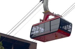Red gondola cabin suspended midair by a crane, part of a cable car system above a building.