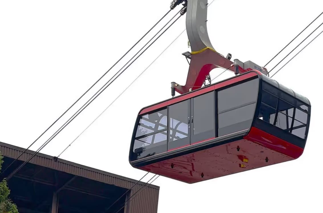 новые кабины grouse grind | Наш Ванкувер Red gondola cabin suspended midair by a crane, part of a cable car system above a building.