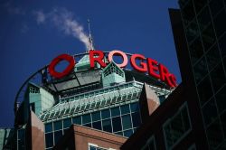 Rogers sign atop a modern teal glass building against a clear blue sky.