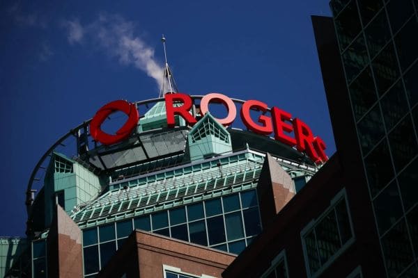 Rogers sign atop a modern teal glass building against a clear blue sky.