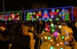 Crowd gathered at night in front of a storefront lit with colorful neon Christmas decorations.