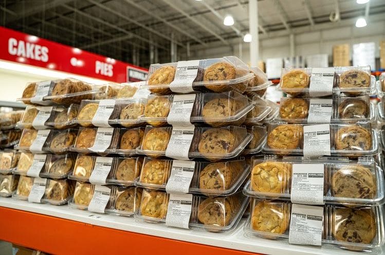 Сахар | Наш Ванкувер Stacks of prepackaged cookies in clear plastic containers on a supermarket bakery display near a cakes and pies sign.