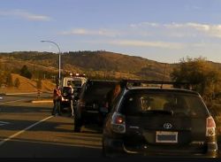 Black Toyota SUV parked on a highway with its rear hatch open, a person nearby, and a tow truck in the background against brown hills under a blue sky.