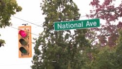 Green street sign reading 'National Ave' beside a red traffic light and utility wires.