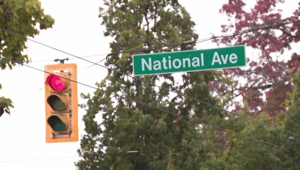 Green street sign reading 'National Ave' beside a red traffic light and utility wires.