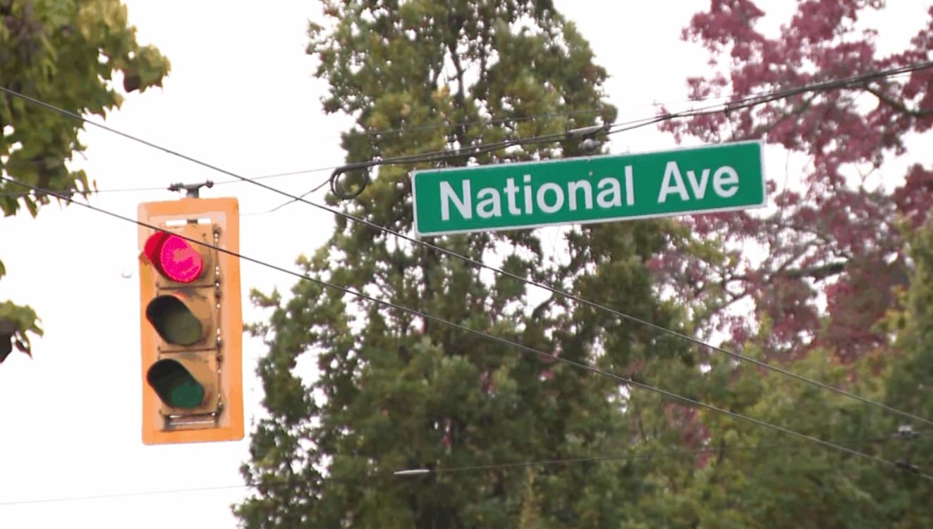 Green street sign reading 'National Ave' beside a red traffic light and utility wires.