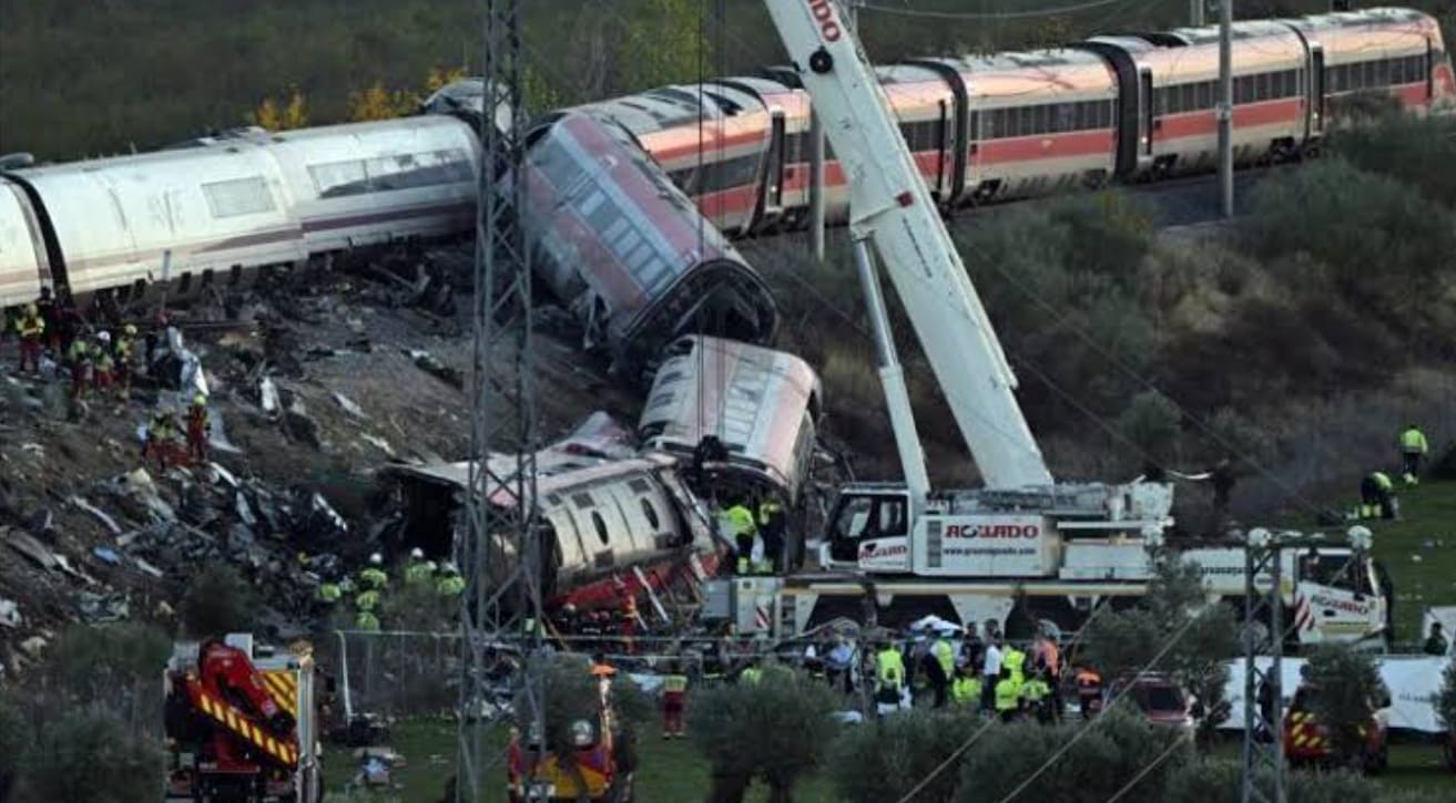 Train derailment scene with overturned passenger cars and emergency responders at the crash site, a crane lifting debris nearby to assist rescue.