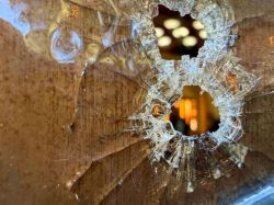 Close-up of a shattered glass surface with two bullet-hole-like holes and radiating cracks, revealing a warm-lit interior beyond.
