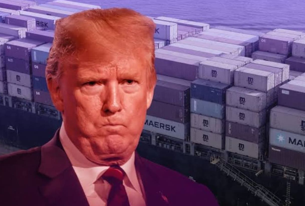Frontal portrait of former President Donald Trump with a stern expression, set against a port with stacked shipping containers in the background.
