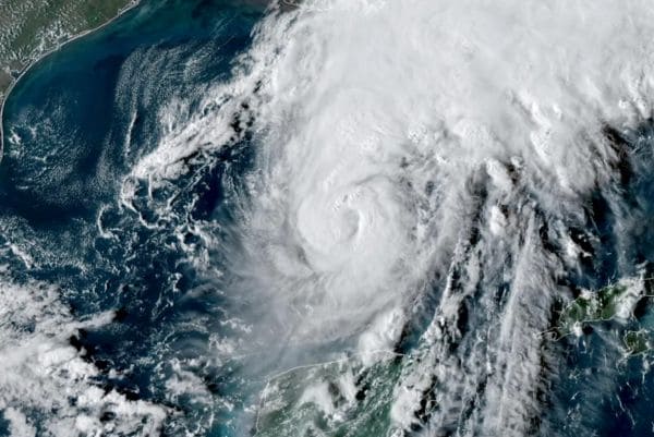 Satellite image of a powerful hurricane with a clear eye over the Atlantic near the U.S. coast, spiraling clouds and heavy storm bands.