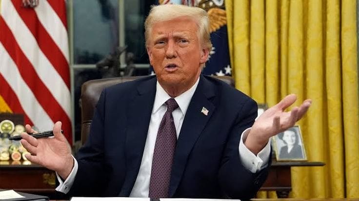 Введении тайных пошлин против США | Наш Ванкувер Man in a dark suit and red tie speaks at a desk with flags behind him, gesturing with open hands.