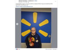 Older man with a name badge holding a bouquet of flowers in front of a blue Walmart backdrop with the yellow Walmart sunburst logo, celebrating an anniversary.